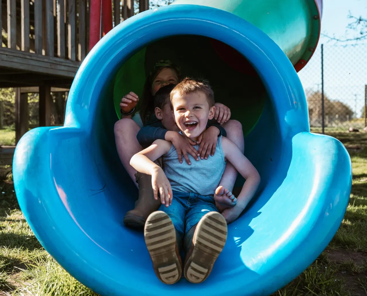 Two young children laughing together inside a bright blue playground tunnel.