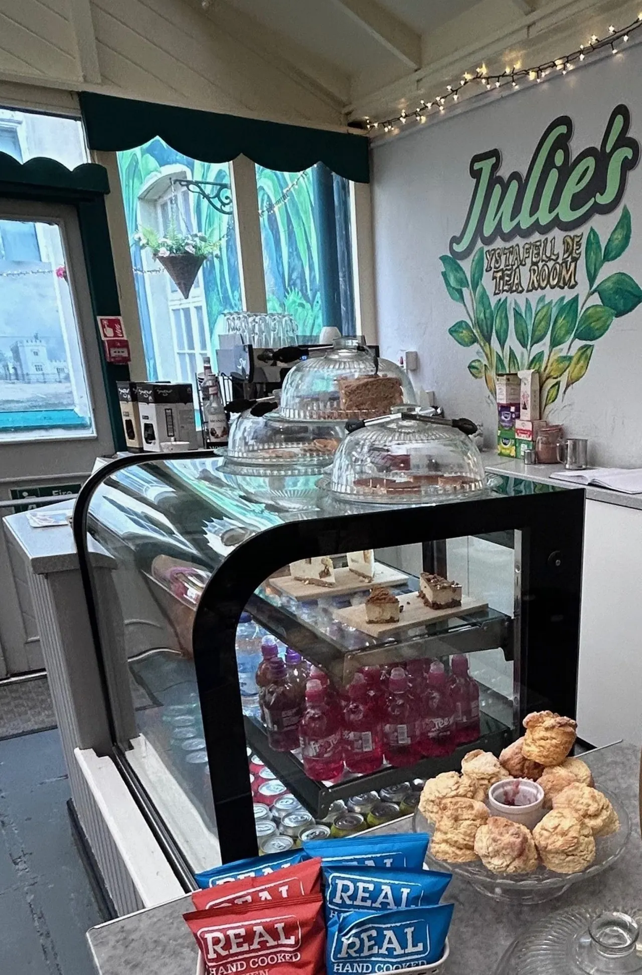 Interior of a tea room with display cases of cakes and baked goods, beverages, and branded packaging on counters.