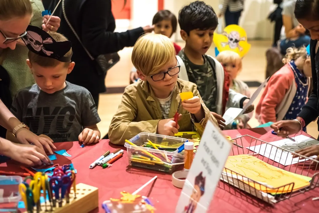 Children at a craft activity table with colouring supplies and materials during an indoor workshop or event.