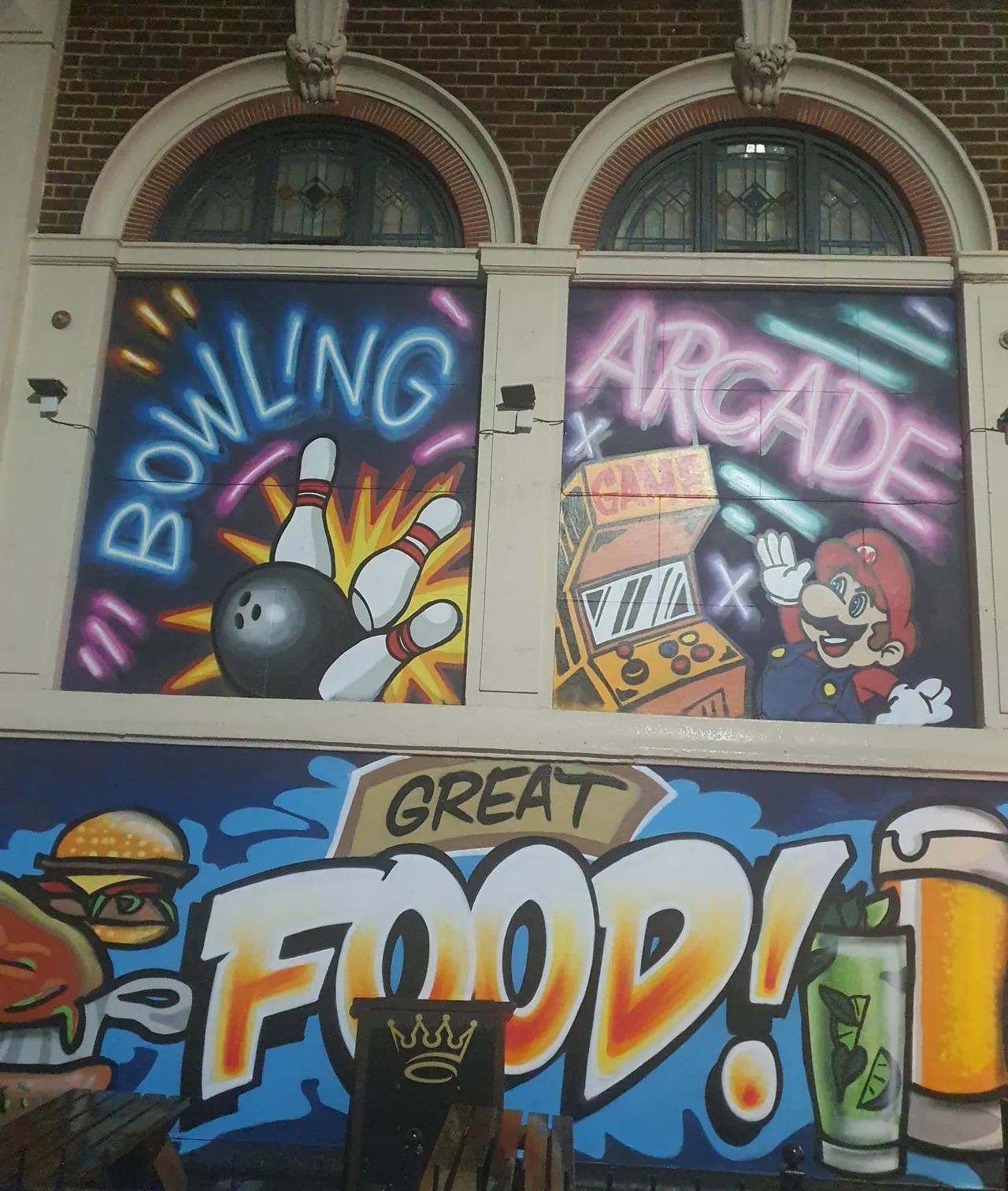Storefront windows display neon signs advertising bowling and arcade games, with colourful graphics below showing food and drink.