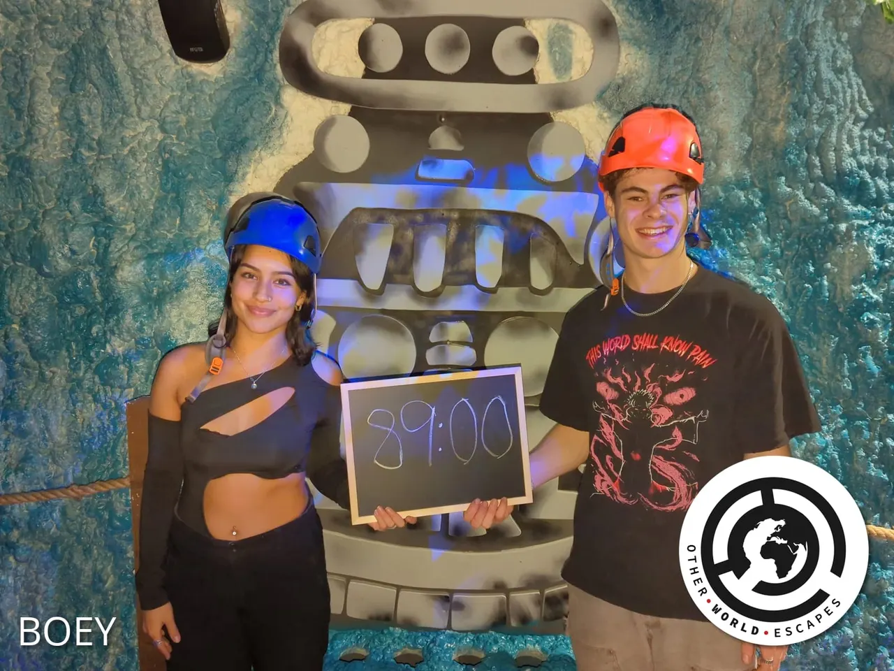 Two people wearing coloured hard hats hold a scoreboard displaying 39:00 in front of a large robot prop with illuminated blue lighting.