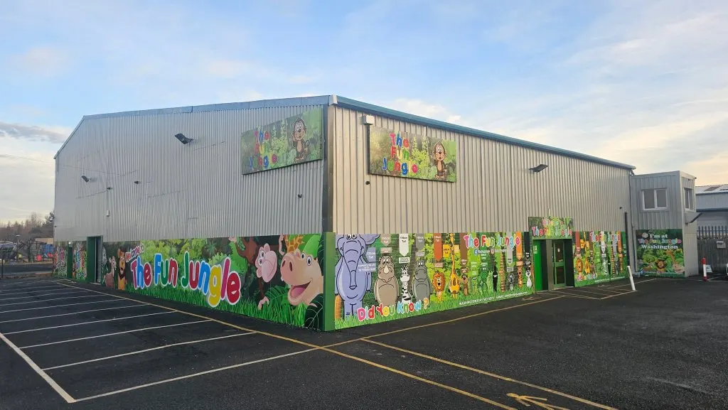Colourful children's play venue building with bright murals featuring cartoon characters and animals on its corrugated metal exterior.