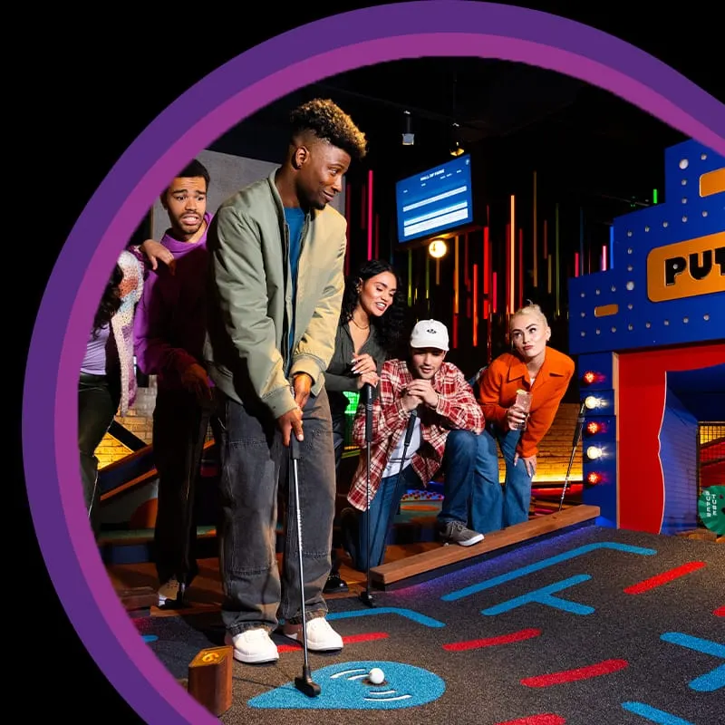 A family playing mini golf indoors with colourful neon-lit course features and arcade-style theming.