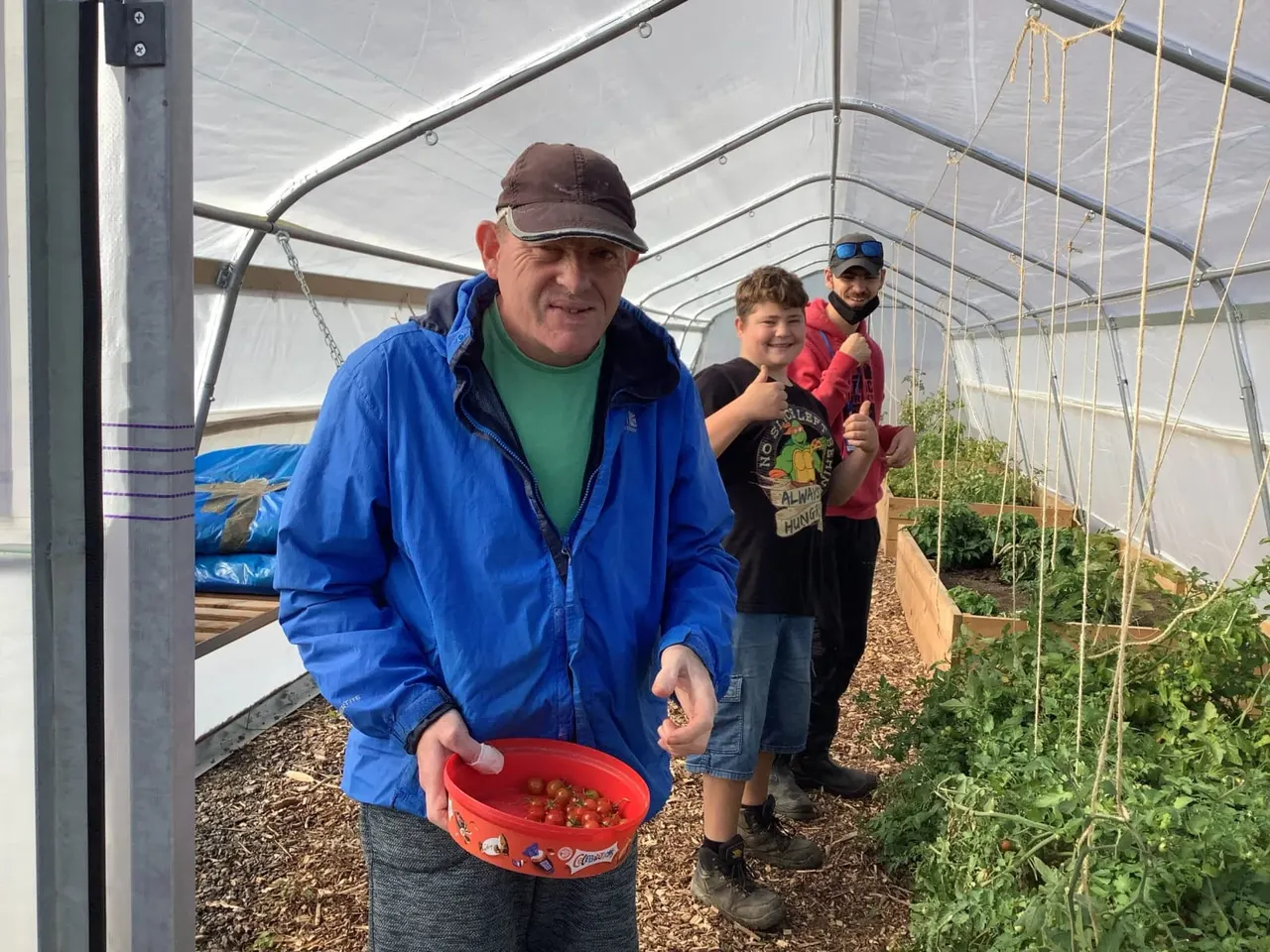 An adult and three children inside a polytunnel holding a red basket of freshly picked strawberries.