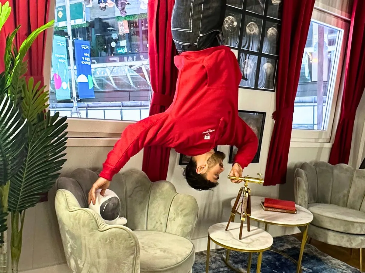 Person doing a headstand on a grey armchair in a red-curtained room with vintage décor.