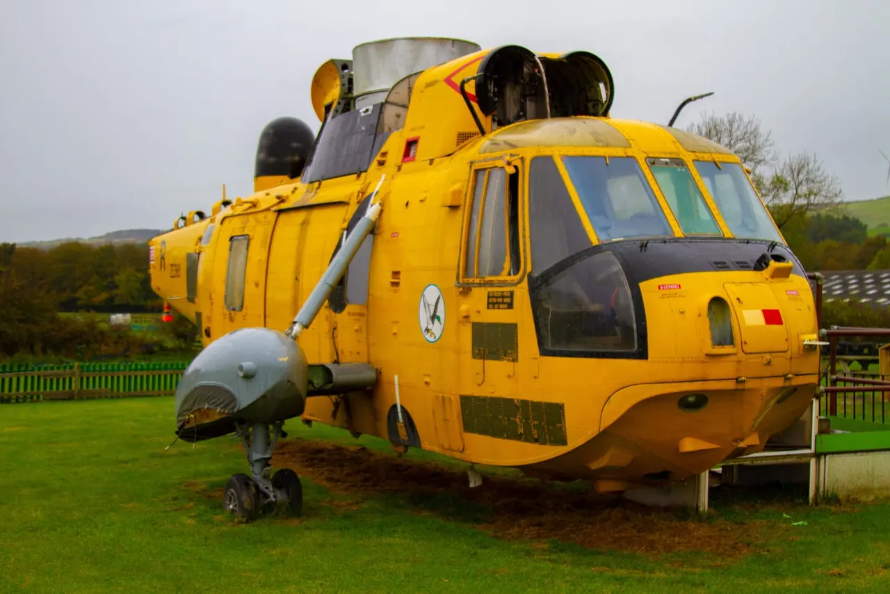 Restored yellow helicopter displayed on grass in a rural park setting.