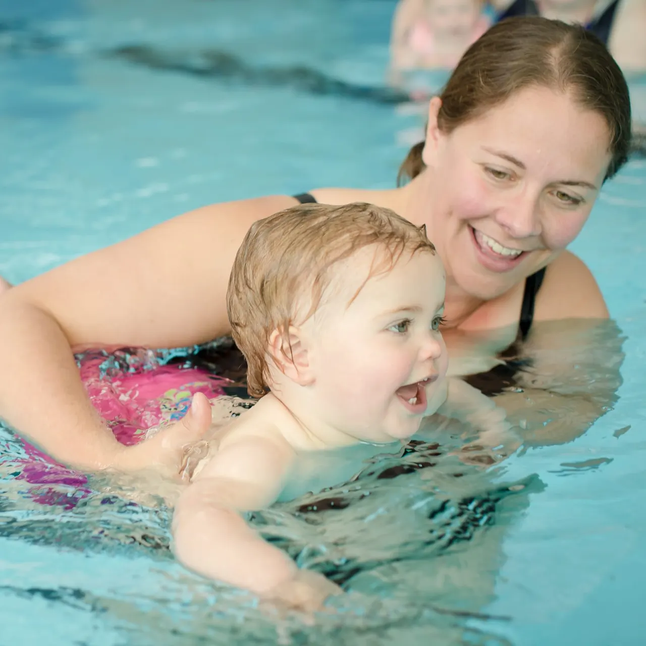 Woman supporting a toddler in a swimming pool during a swim lesson.