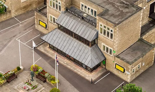 Aerial view of a stone building with a modern metal-clad theatre entrance and street-level forecourt with planted areas.