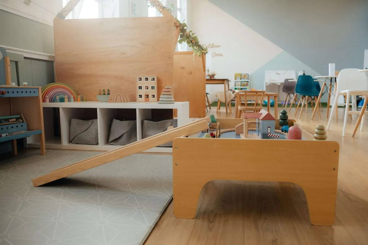 Bright, airy playroom with wooden play structures, storage cubbies, toy displays, and natural light from skylights.