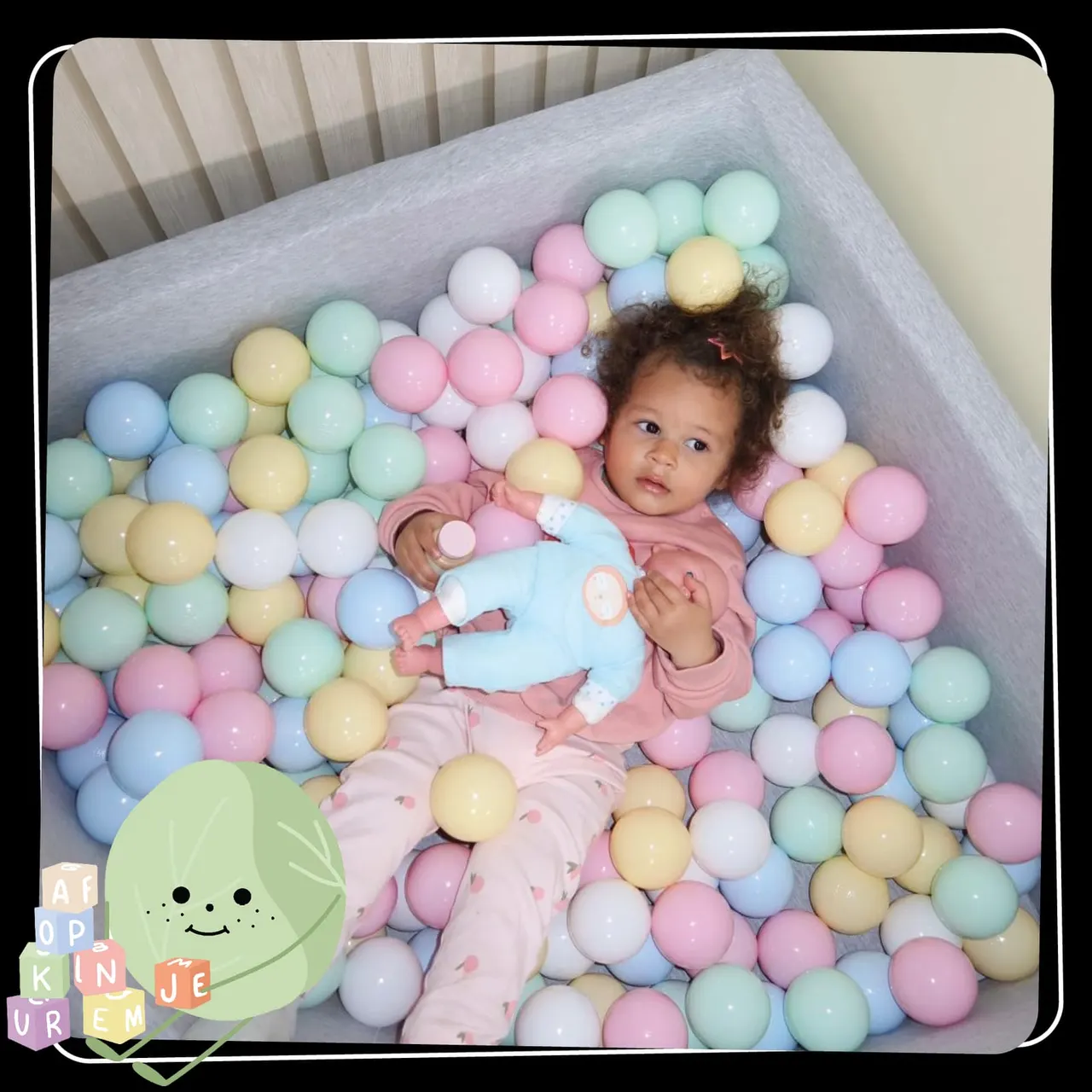 Toddler lying in a ball pit filled with pastel-coloured balls, looking at camera.