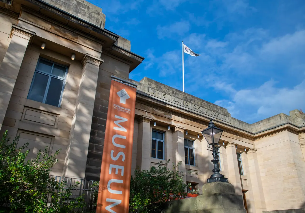 Classical stone museum building with orange banner and flag against blue sky.