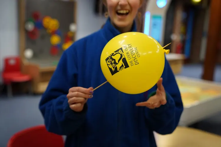 Child in blue jacket holding a yellow balloon indoors at a leisure centre.