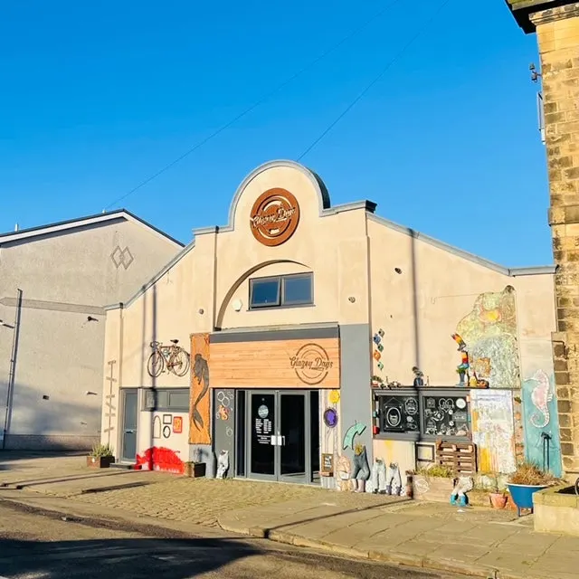 Cream and beige building with arched roof and circular logo, decorated with colourful street art and a bicycle outside.