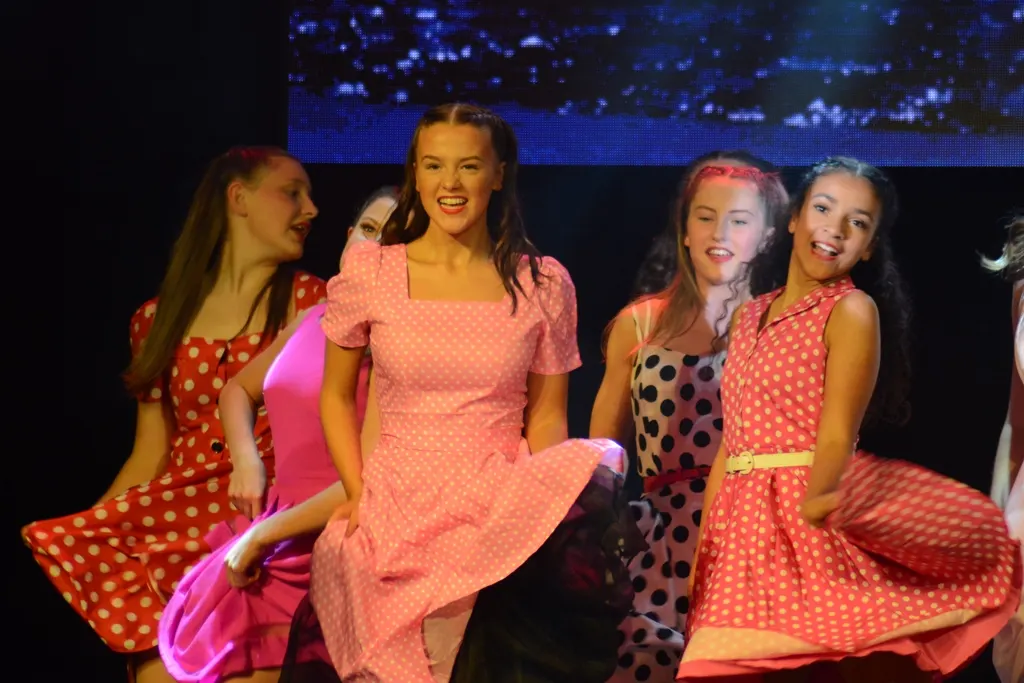 Young performers in colourful polka-dot dresses dancing on stage during a theatrical production.
