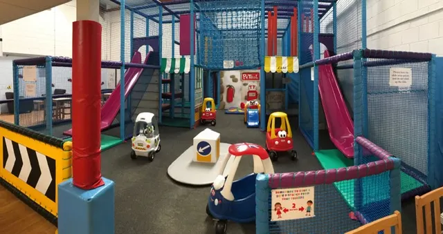 Indoor play area with colourful climbing structures, slides, and toy vehicles for young children.