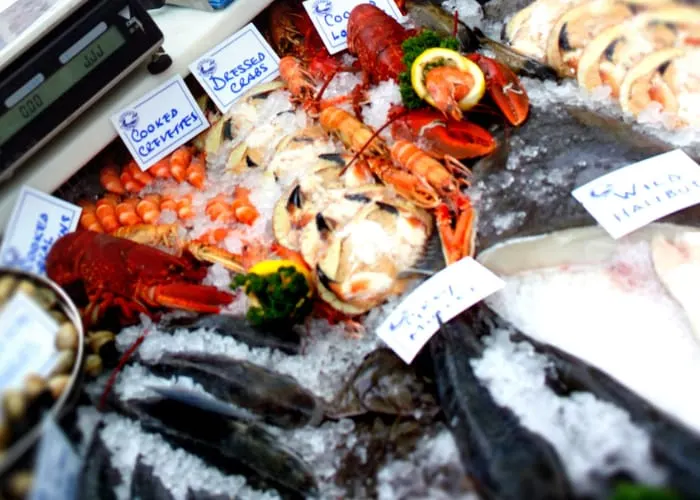 A seafood display on ice showing lobsters, shellfish and fish with handwritten price labels.