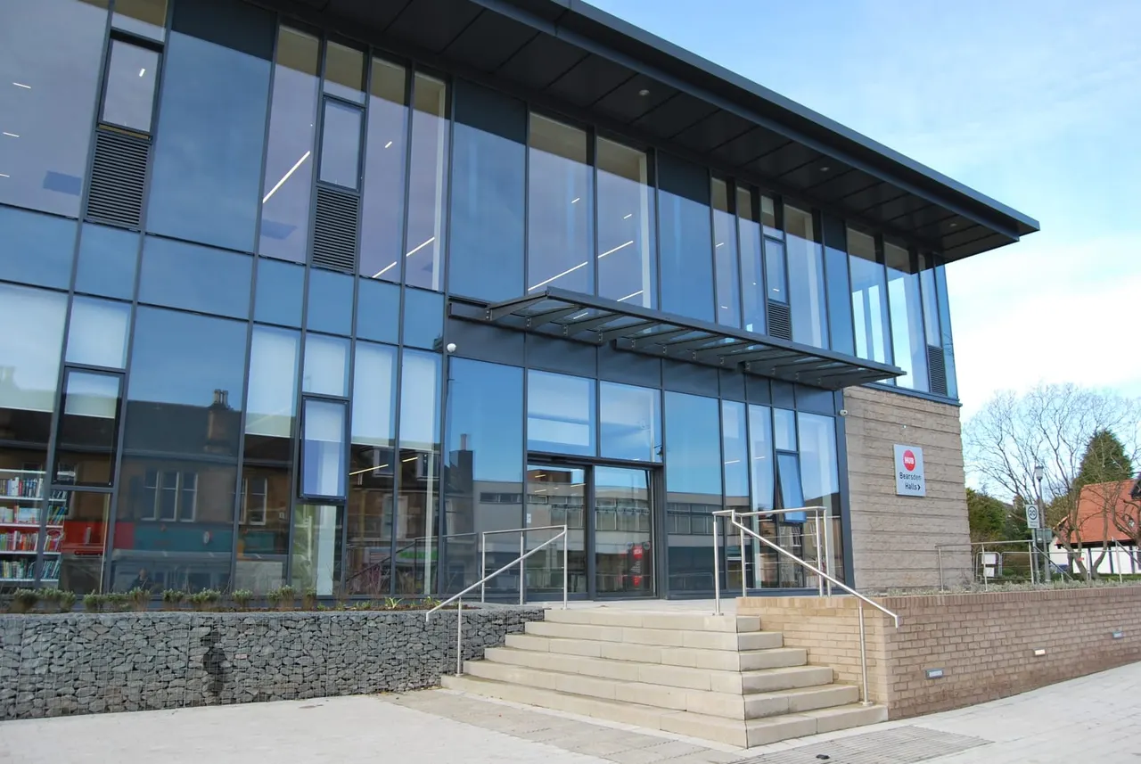 Modern leisure centre exterior with glass façade, stone steps leading to entrance, and brick base wall.