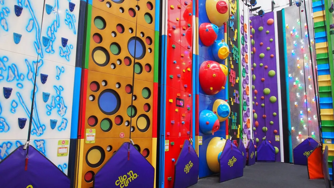 Colourful indoor climbing walls with large handholds and holds of various colours, with inflatable safety bases below.
