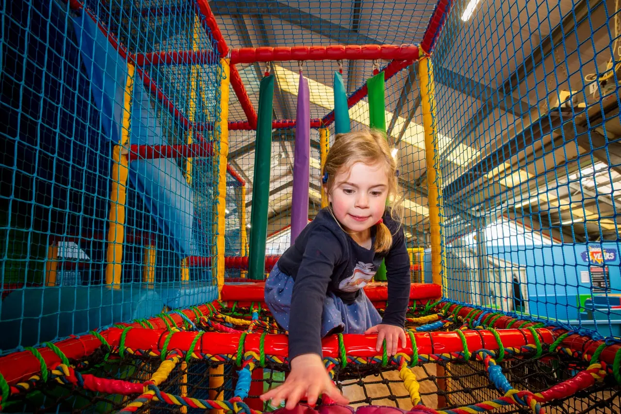 Young child crawling through a colorful soft play structure with netting and foam obstacles.
