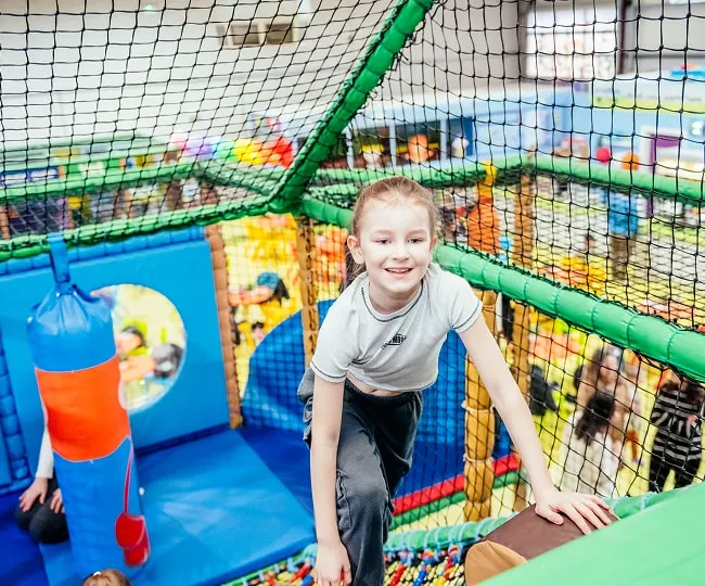 Child smiling inside a colourful soft play structure with netting and foam obstacles.