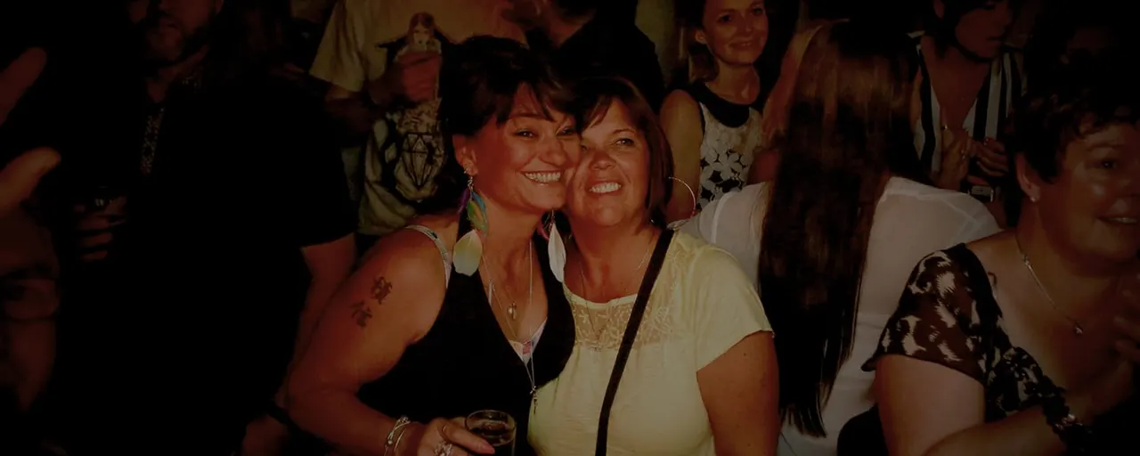 Group of smiling women socialising and enjoying drinks together at an evening event indoors.