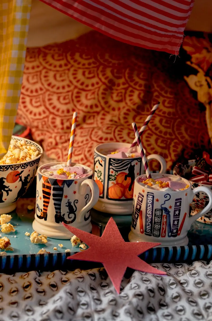 Themed mugs with striped straws containing pink drinks topped with popcorn, arranged on a colourful surface with a red star.