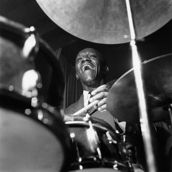 Drummer performing energetically at a drum kit during a jazz performance.