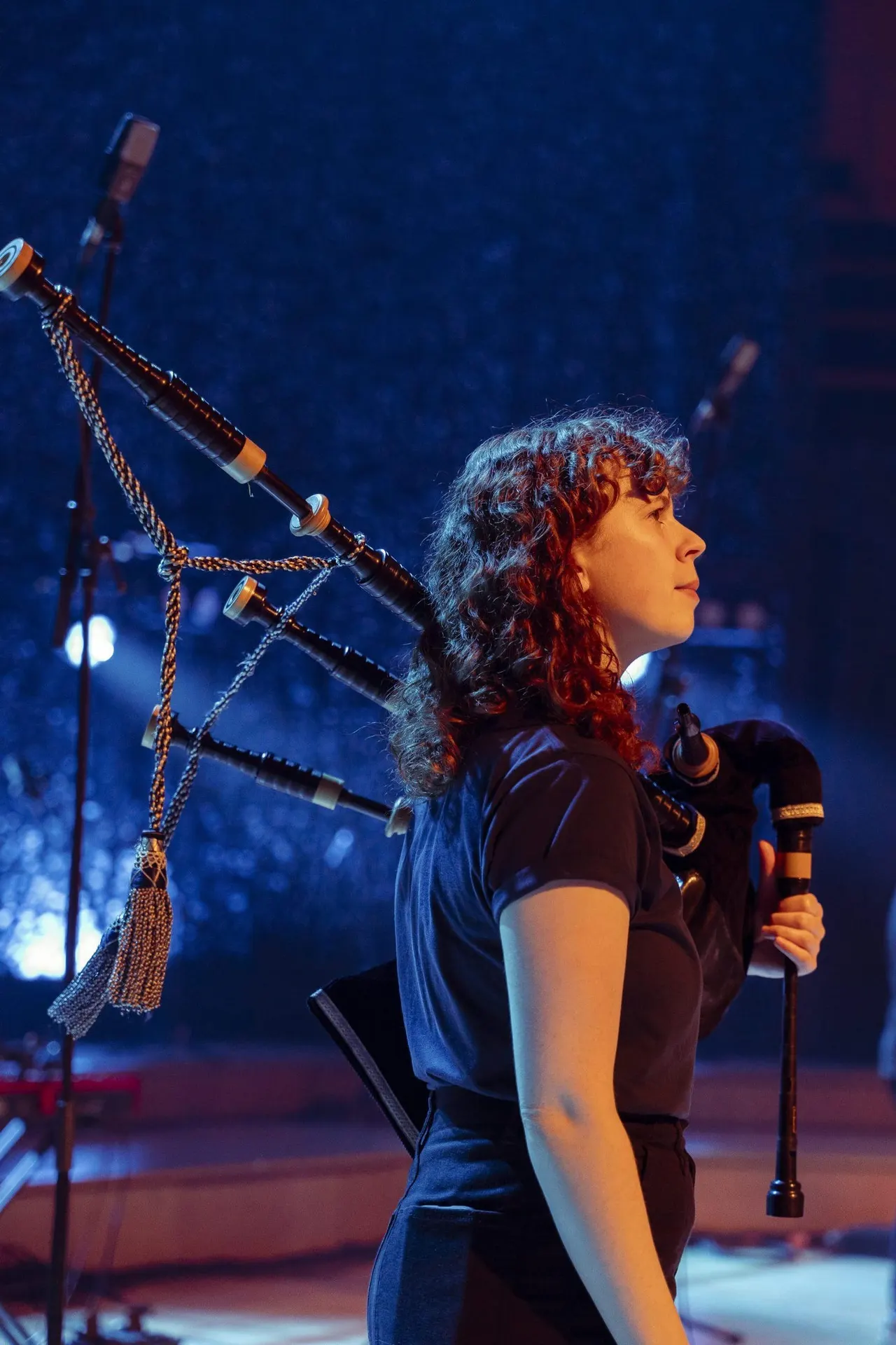 Musician playing bagpipes on stage with atmospheric blue lighting.
