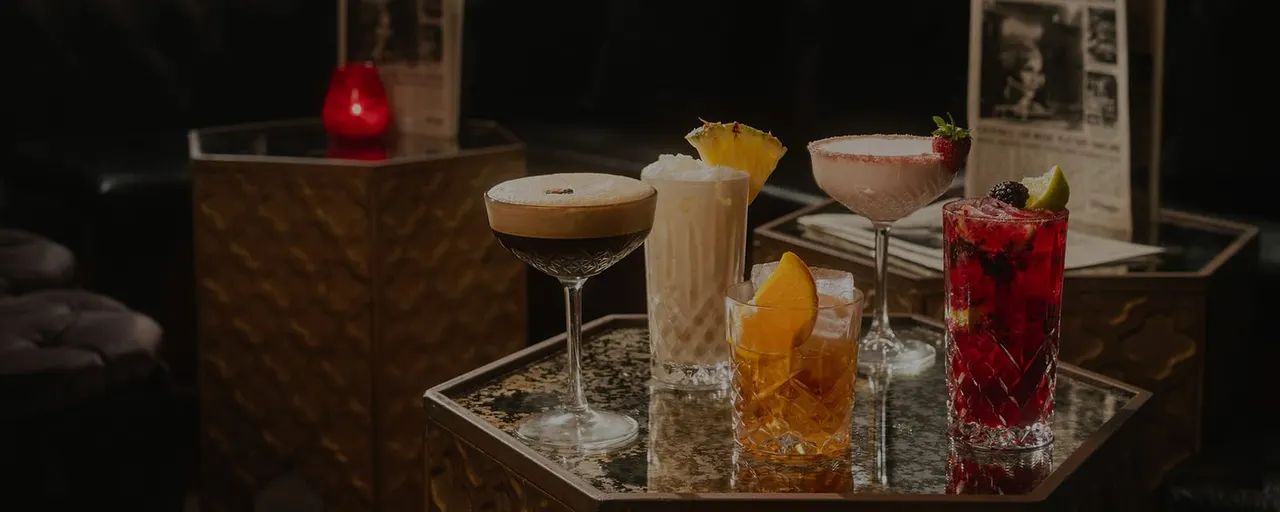 Array of cocktails on a table in an upmarket bar setting, including a martini, highballs and a berry-garnished drink.