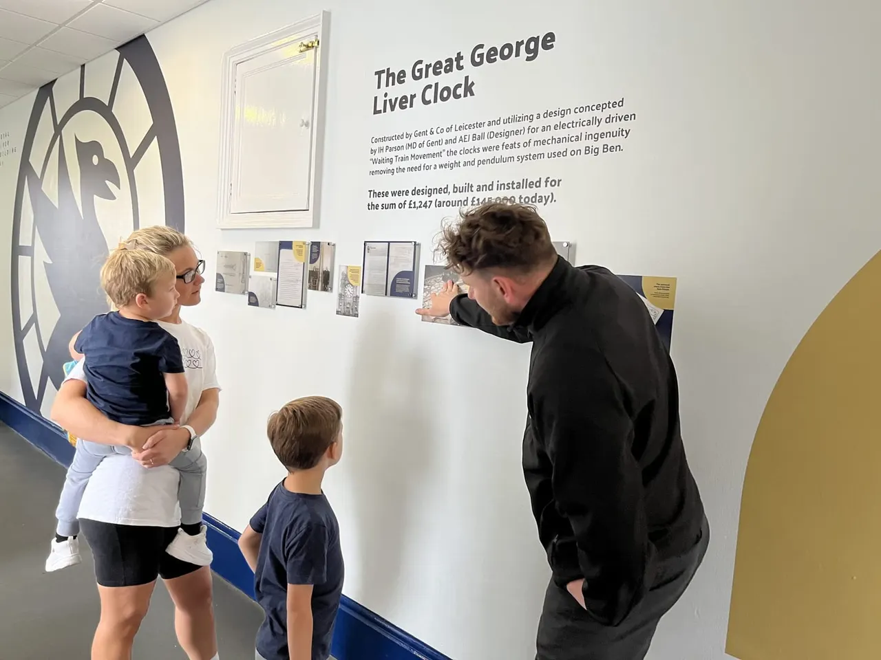 Family viewing an exhibition display about the Great George Liver Clock at an indoor museum or heritage venue.