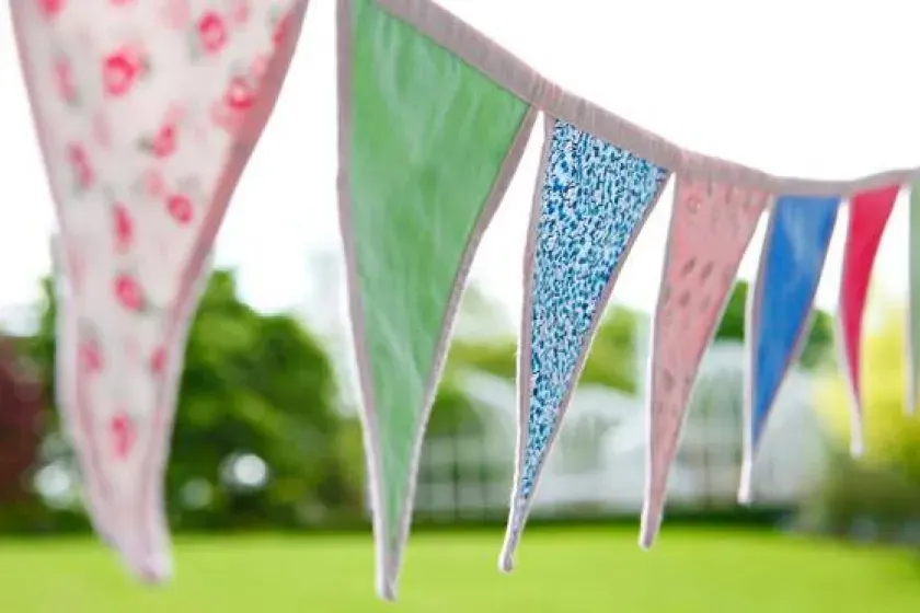 Colourful bunting with pink, green, blue and red patterned flags strung across a garden lawn.