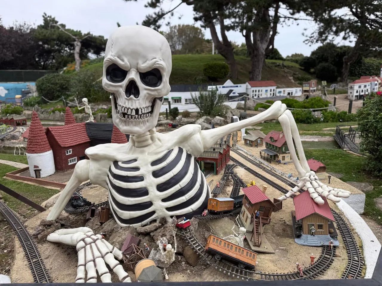 Giant skeleton structure looming over miniature railway village and buildings display.