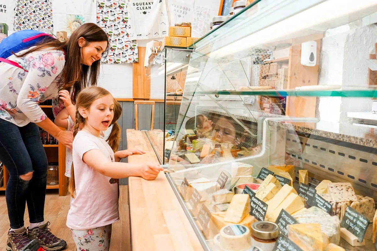 A woman and young girl look at farm animals in glass enclosures during an indoor visit.
