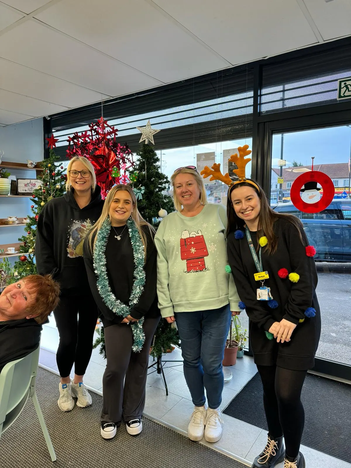 Five people smiling at the camera in an indoor space decorated with Christmas ornaments and garlands.