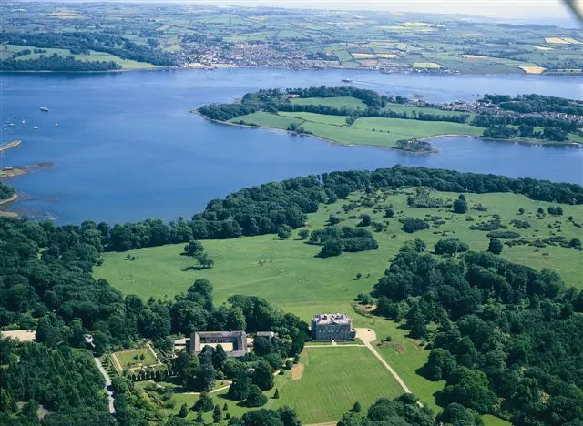 Aerial view of a large freshwater lake surrounded by green fields, woodlands, and rural settlements with a castle visible in the foreground.