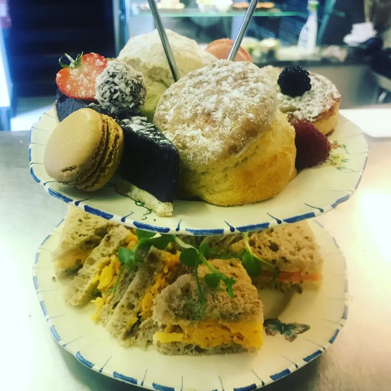 Afternoon tea tiered stand with savoury sandwiches on lower plate and sweet pastries, macarons and fresh berries on upper plate.