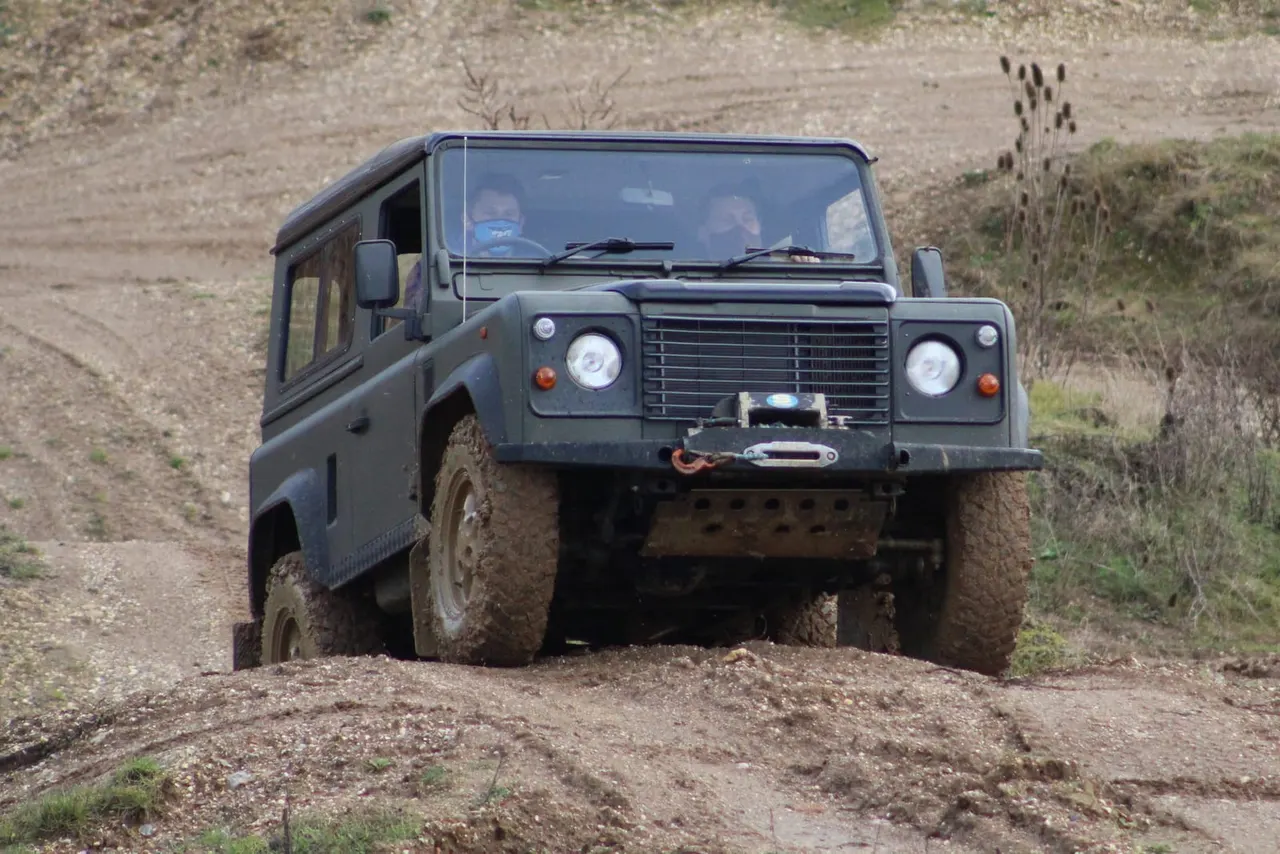 A khaki four-by-four vehicle driving through mud on a rough off-road track.
