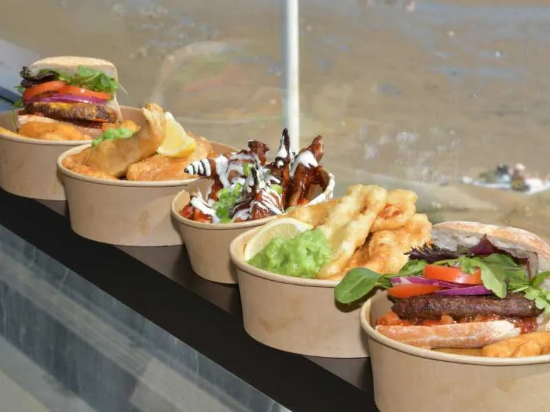 Range of burgers and fried food served in cardboard containers on a counter.