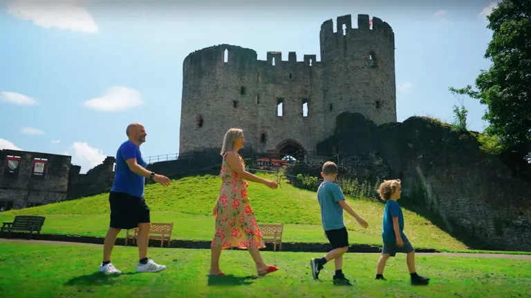 Family playing in grass in front of medieval castle ruins on a sunny day.