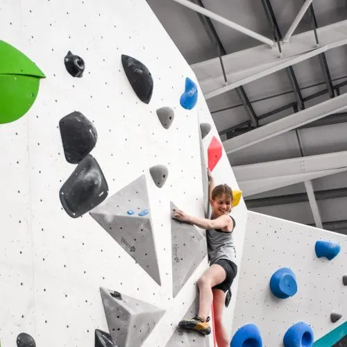 Child climbing an indoor rock wall with various coloured holds in a modern gym facility.