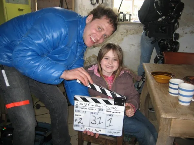 Adult and child on a film set holding a film production clapper board together, smiling at the camera.