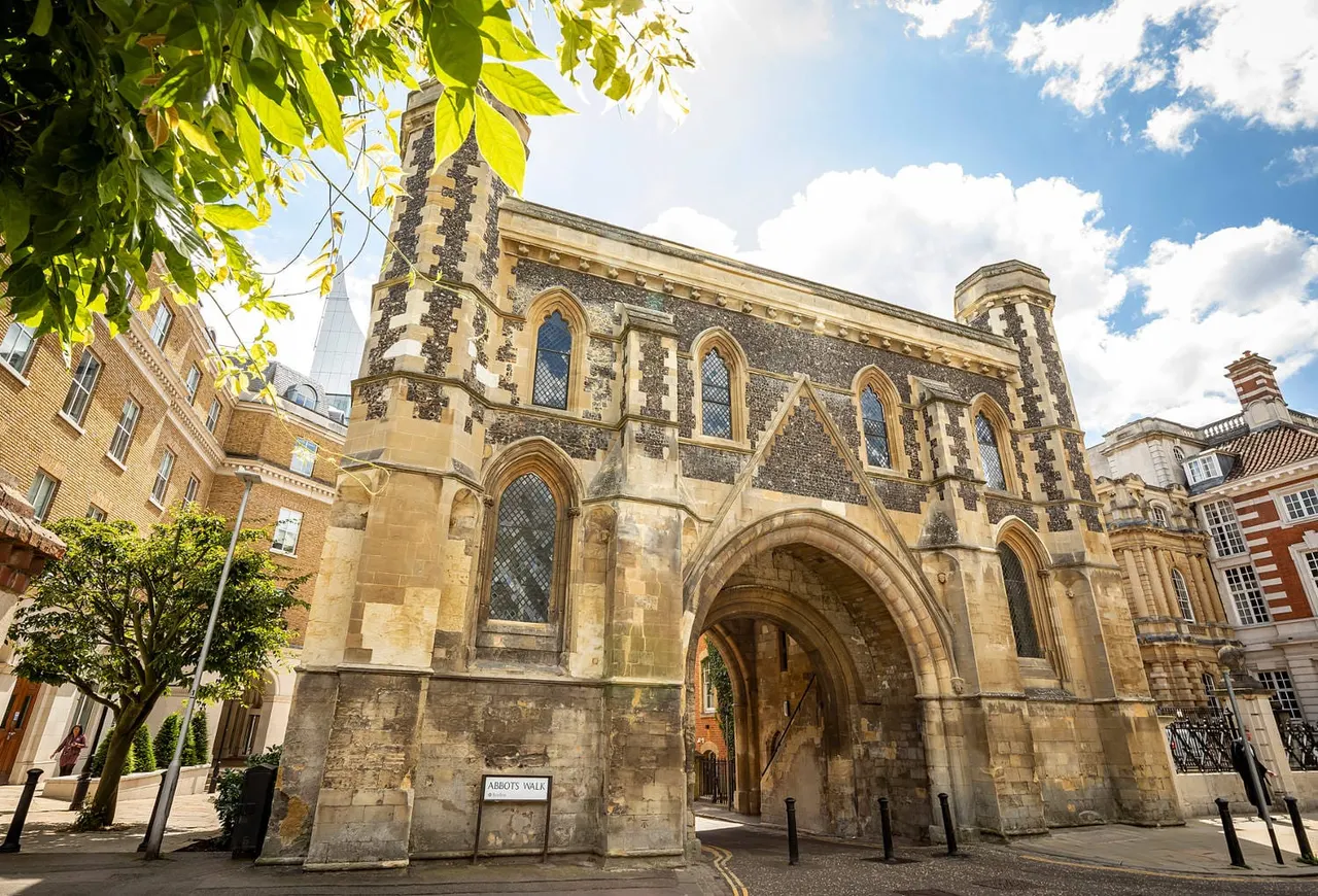 Historic stone church building with arched entrance and tall windows, surrounded by period architecture on a sunny day.