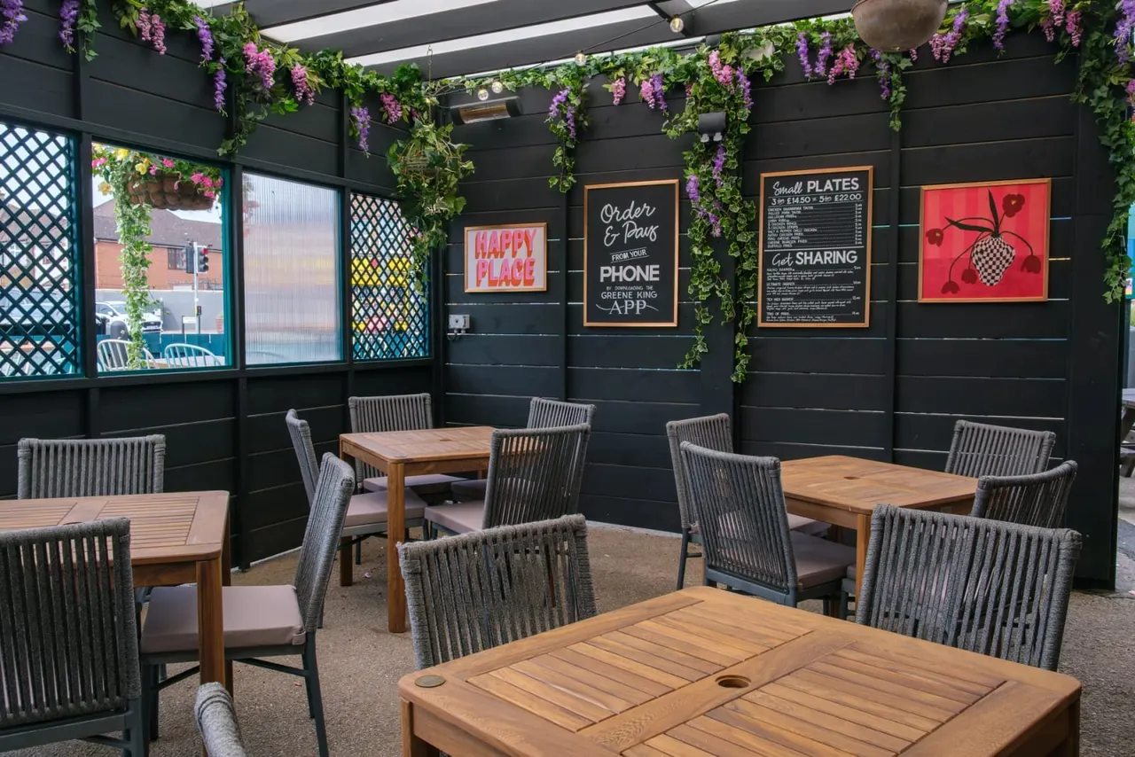 Modern dining area with wooden tables, grey chairs, black walls decorated with hanging purple flowers and ivy, and menu boards.