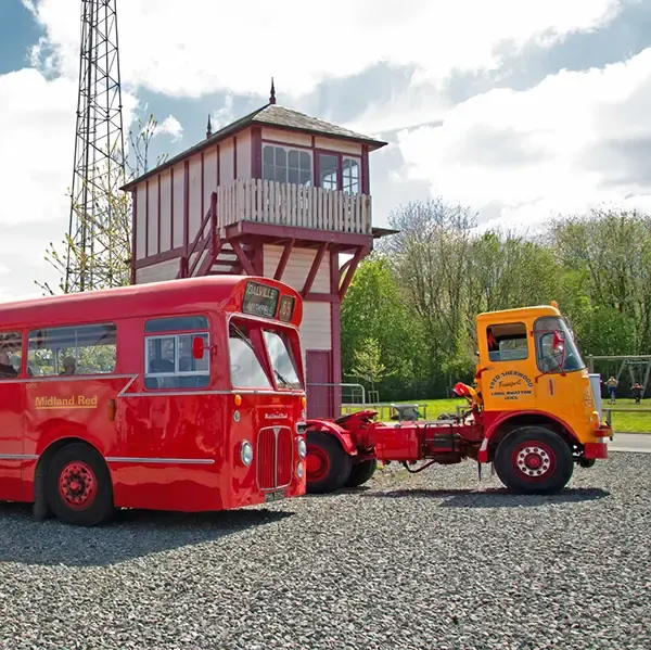 Red and orange vintage vehicles parked beside a red and white elevated signal box under blue sky.