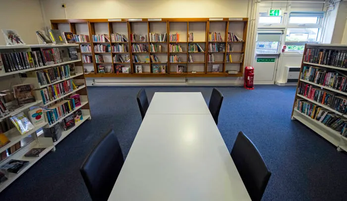 Library reading room with long white table, black chairs and bookshelves lining the walls.