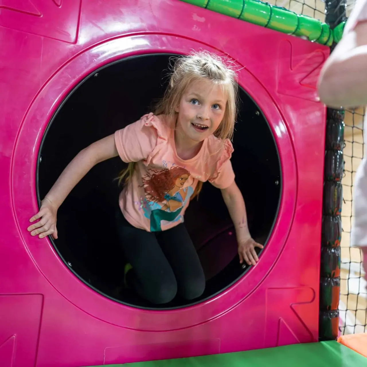 A child crawling through a circular tunnel in a bright pink play structure.