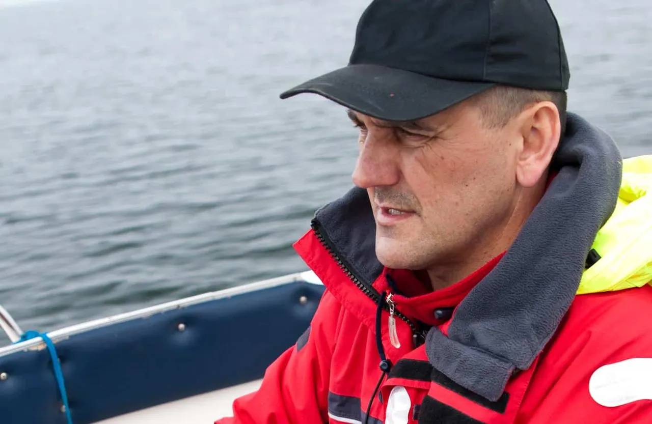 Man in red and black life jacket on a boat looking out at the sea.