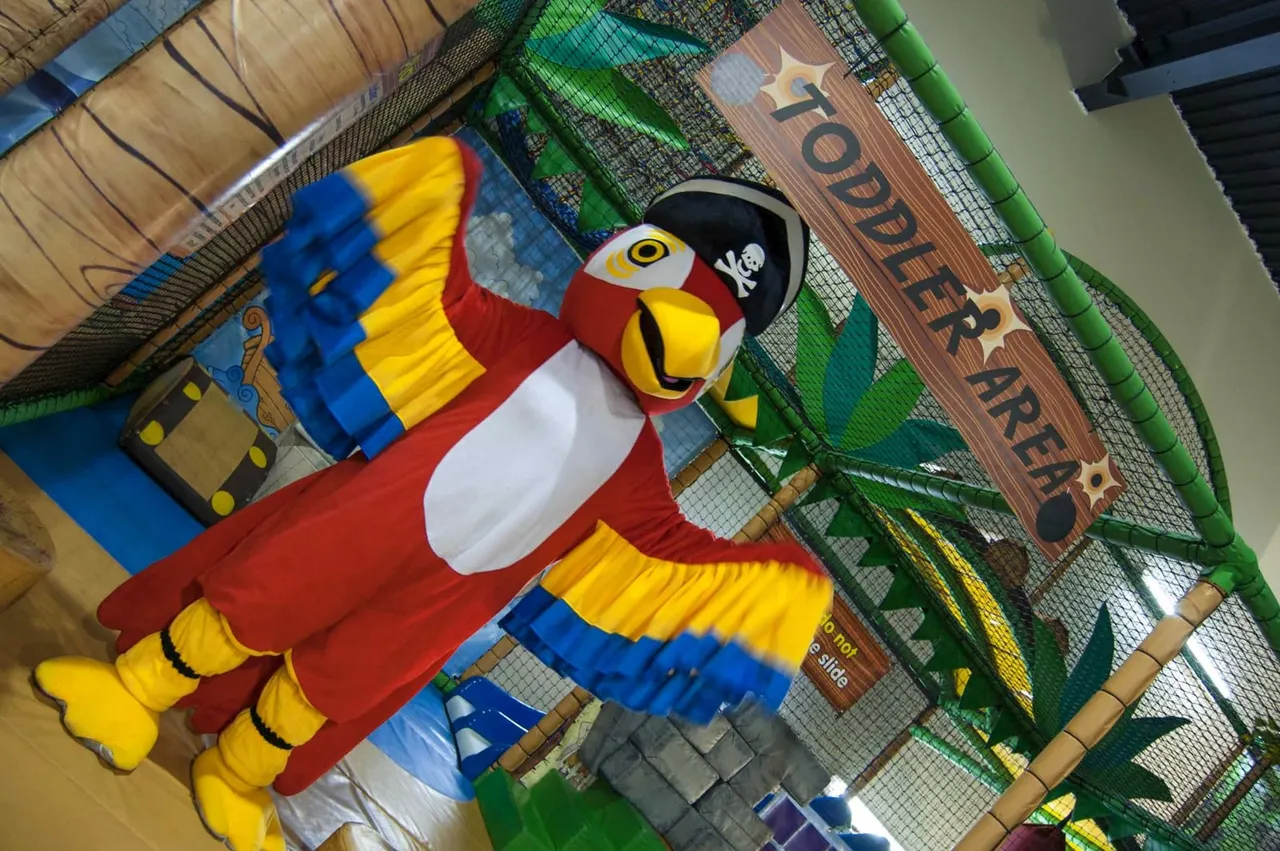 Pirate-themed soft play area with a large colourful parrot character and tropical scenery.