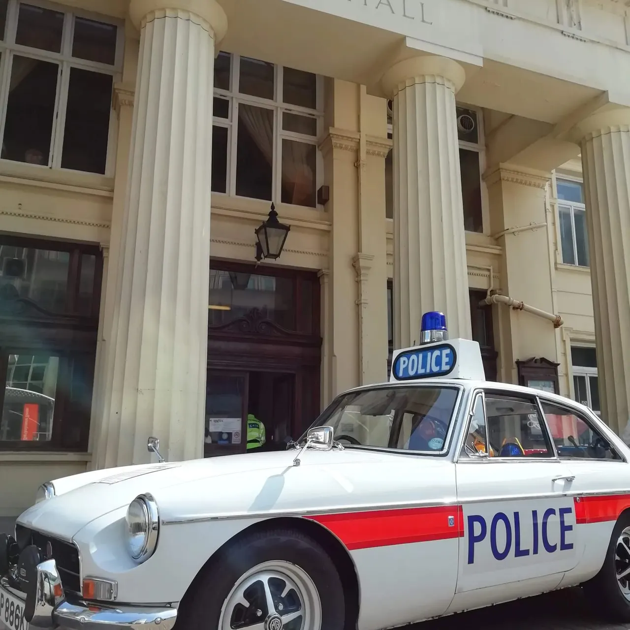 Vintage police car parked outside a neoclassical building with white columns.