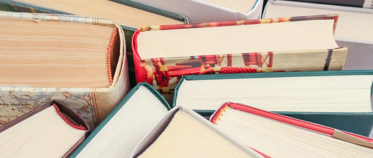 A stack of hardback books with coloured cloth covers and decorative bookmarks.